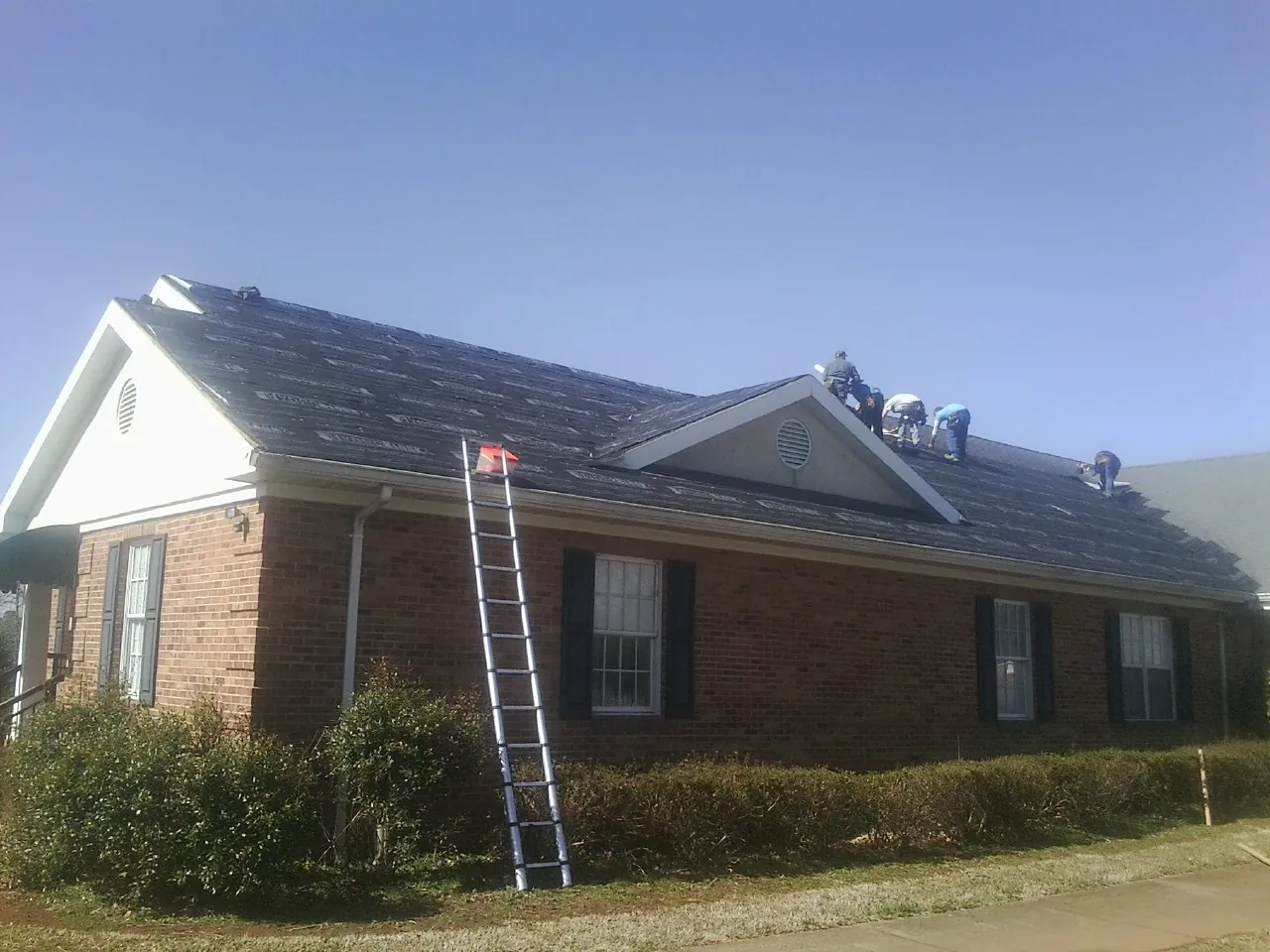 Crew tearing shingles off a brick ranch roof with a ladder set — Metal Roof Repair work by our crew in Mount Sidney