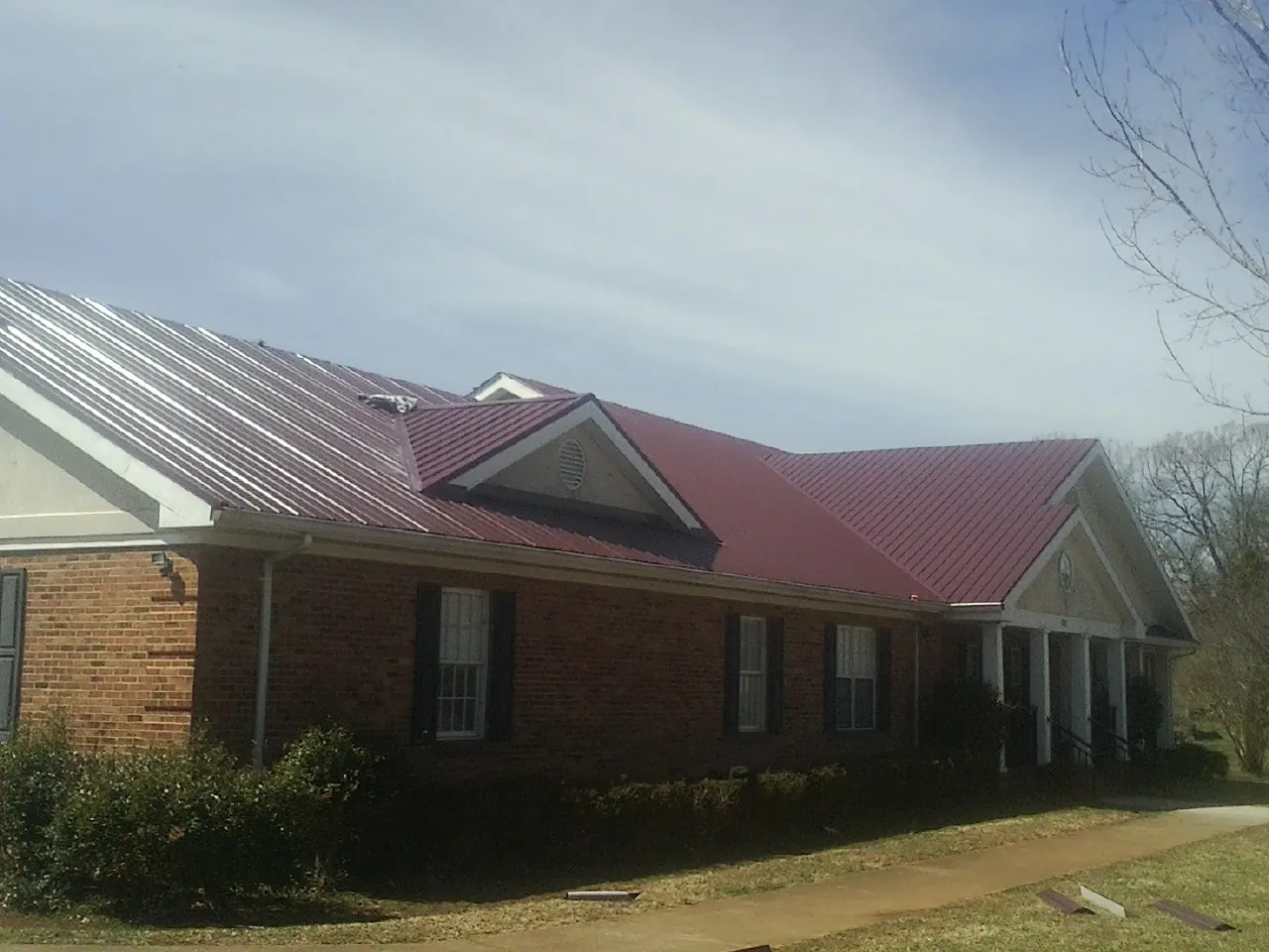 Red metal roof with gabled entries on a long brick building, from a Hail Damage Roof Repair job in Mount Sidney