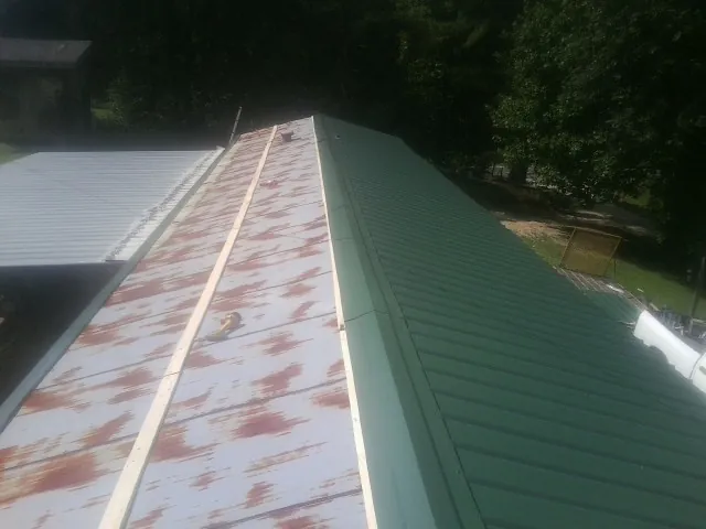 Old rusted panels beside newly installed green metal roofing — Wind Damage Roof Repair by Roofing Brothers in Mount Sidney