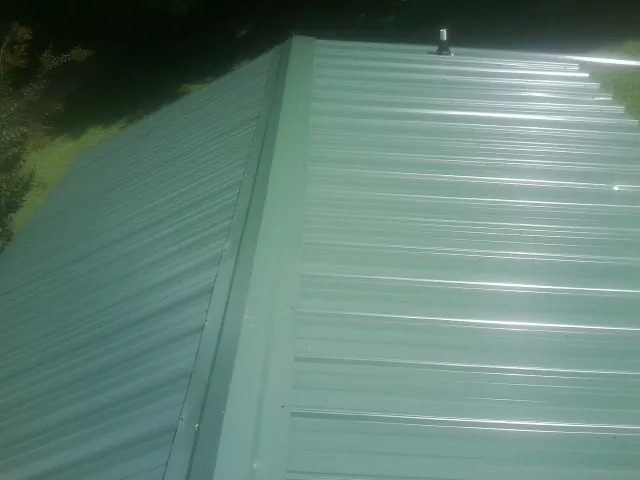 New green metal panels meeting at the ridge of a roof — Flat Roof Repair work by our crew in Mount Sidney